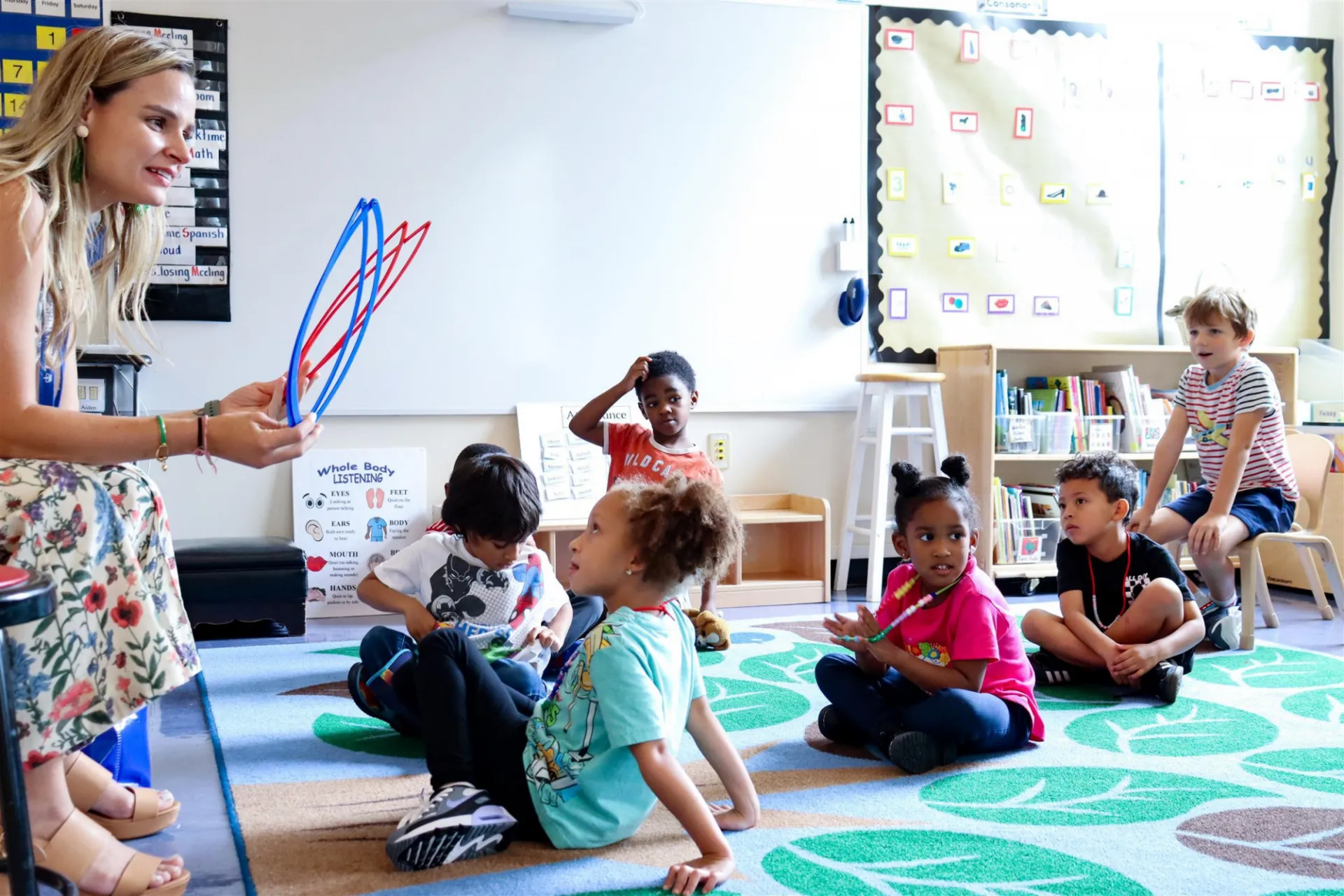 teacher addressing students sitting on a rug